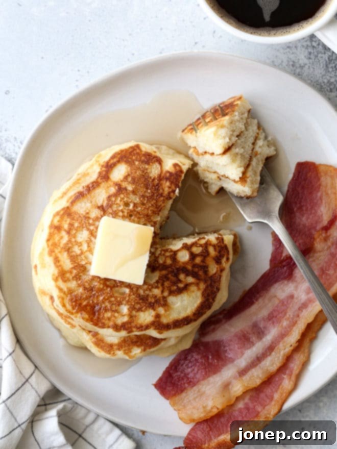 A stack of perfectly golden and fluffy buttermilk pancakes, garnished with berries and syrup.