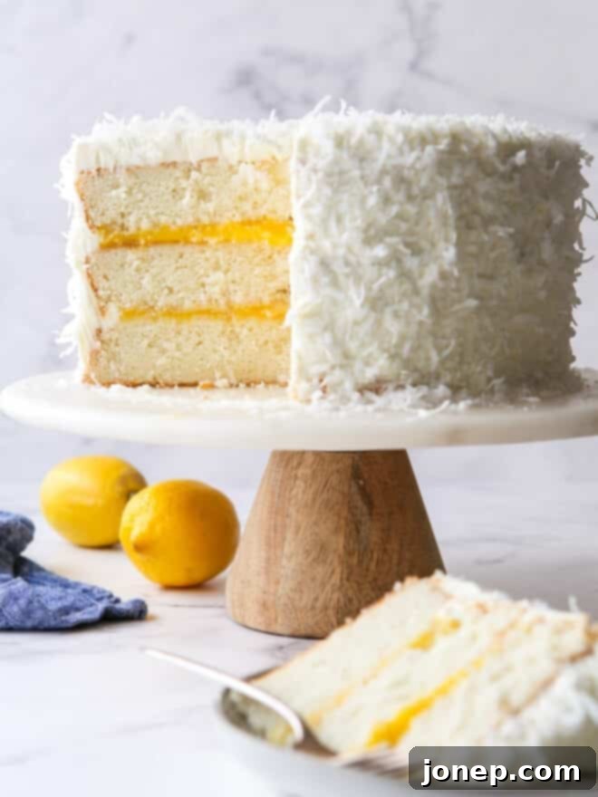 sliced lemon coconut cake on a cake stand, revealing its beautiful layers of cake, lemon curd, and frosting