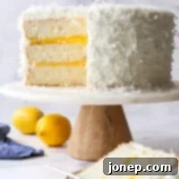 Luscious Lemon Coconut Cake 12 sliced lemon coconut cake on a cake stand with whole lemons nearby