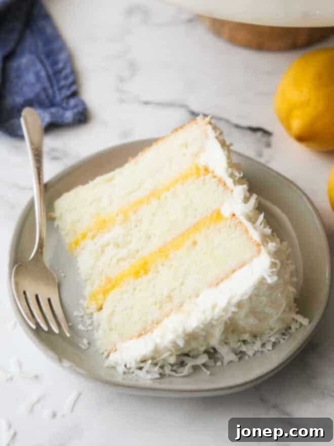 Luscious Lemon Coconut Cake 3 closeup of a slice of lemon coconut cake on a plate, showing the creamy frosting and tender cake