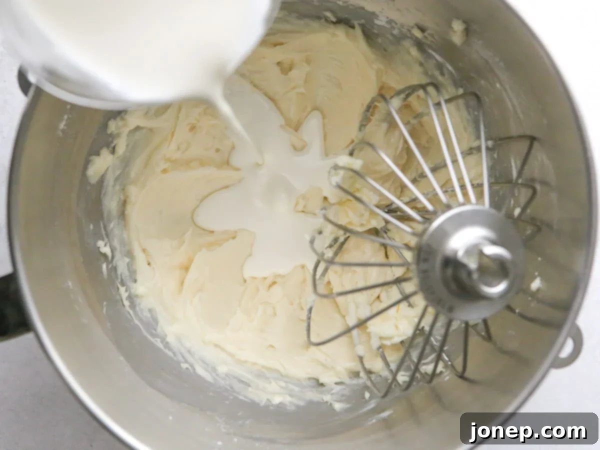 Slowly adding cold heavy cream to the cream cheese mixture in a stand mixer