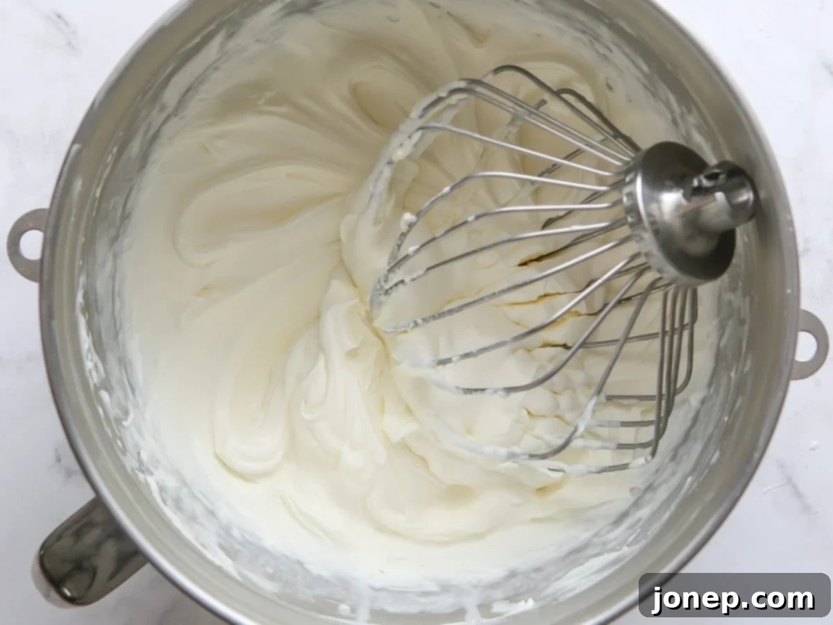 Beautifully whipped Chantilly cream frosting in a mixing bowl with a whisk attachment, showing medium peaks