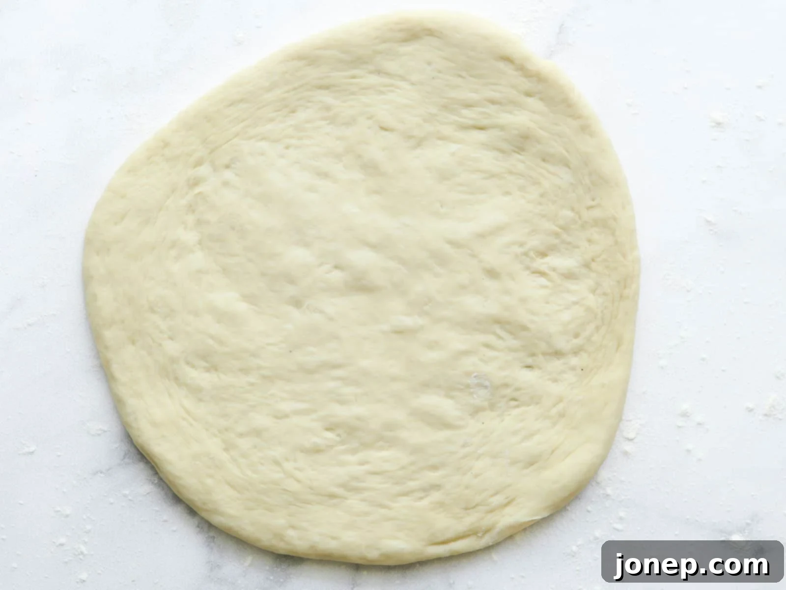 Rolled out pizza dough on counter, perfectly round and thin