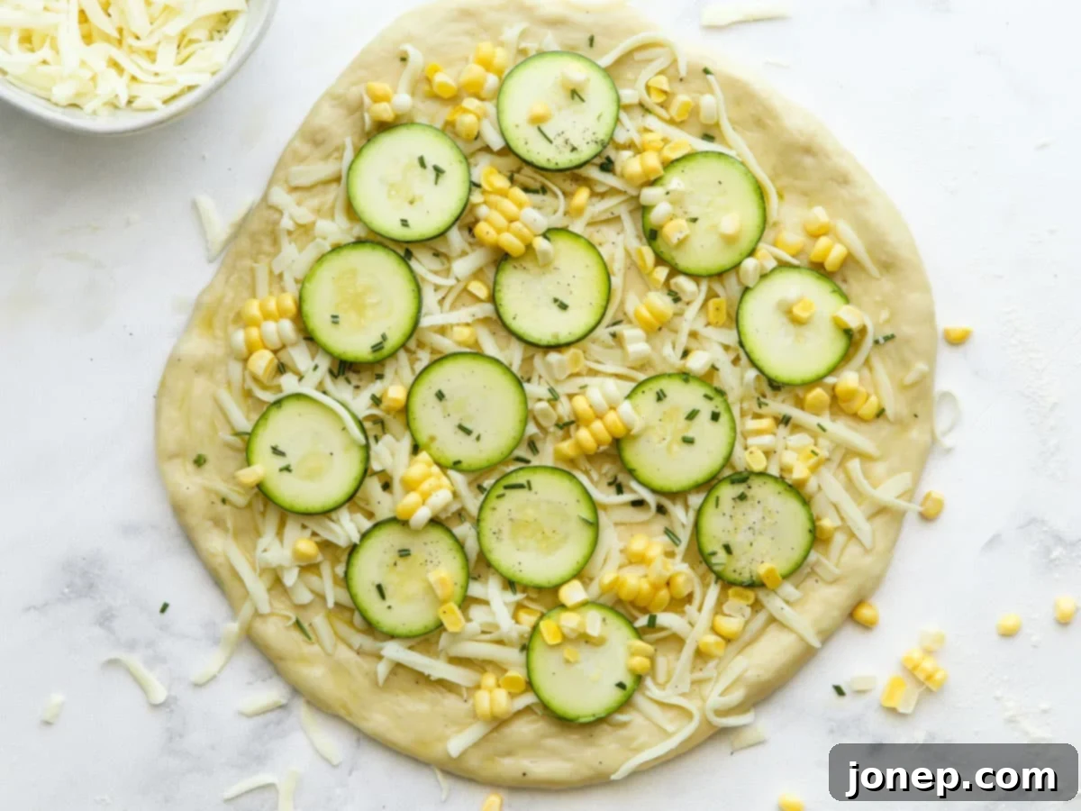 Assembled zucchini corn pizza ready for the oven, topped with cheese, corn, zucchini, and herbs