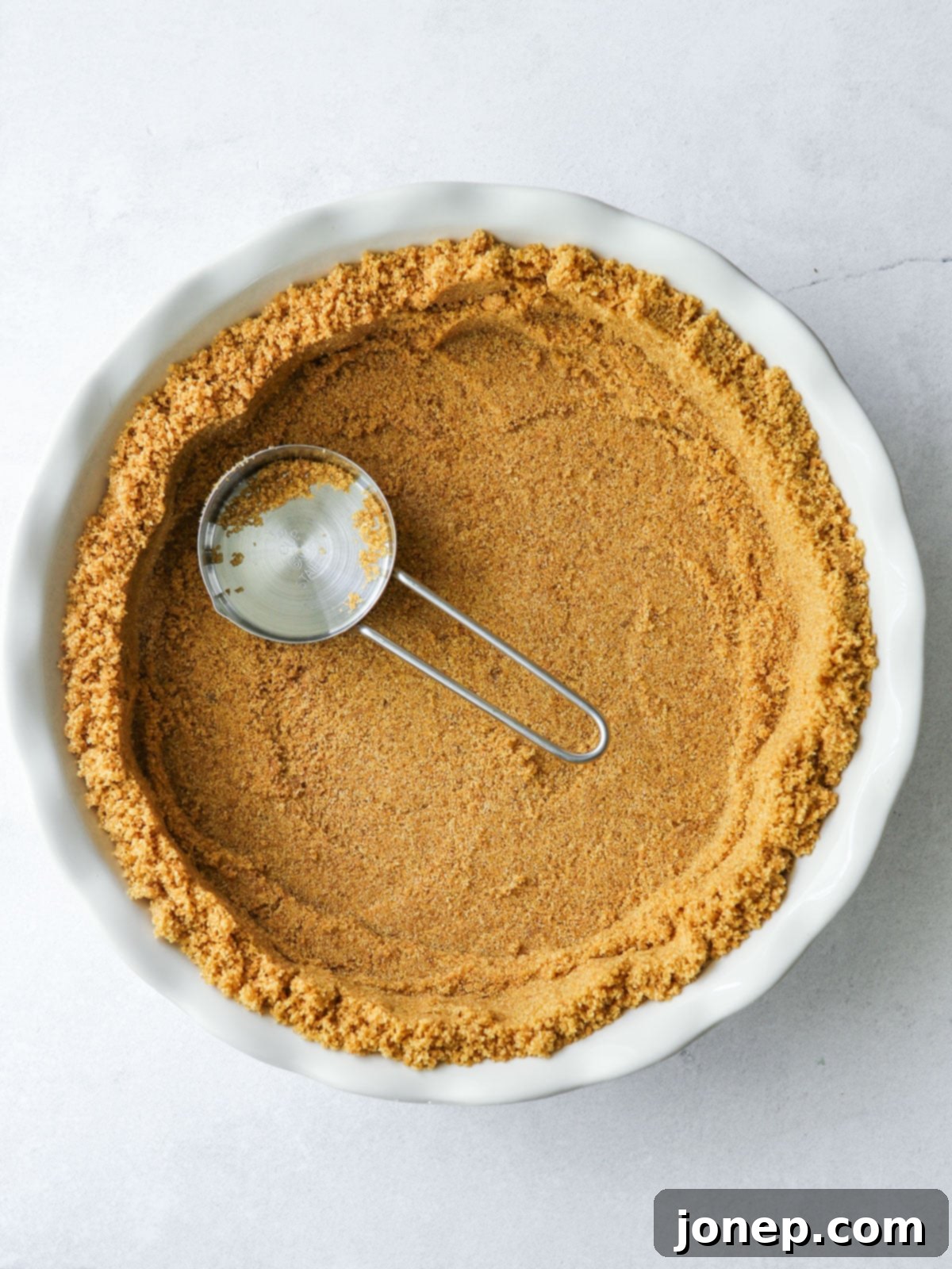 Hands pressing graham cracker crust mixture firmly into a pie pan with the bottom of a measuring cup.