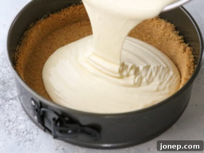 Effortless Water Bath for Flawless Cheesecake 3 Pouring cheesecake filling into a prepared crust in a springform pan, highlighting the preparation stage.
