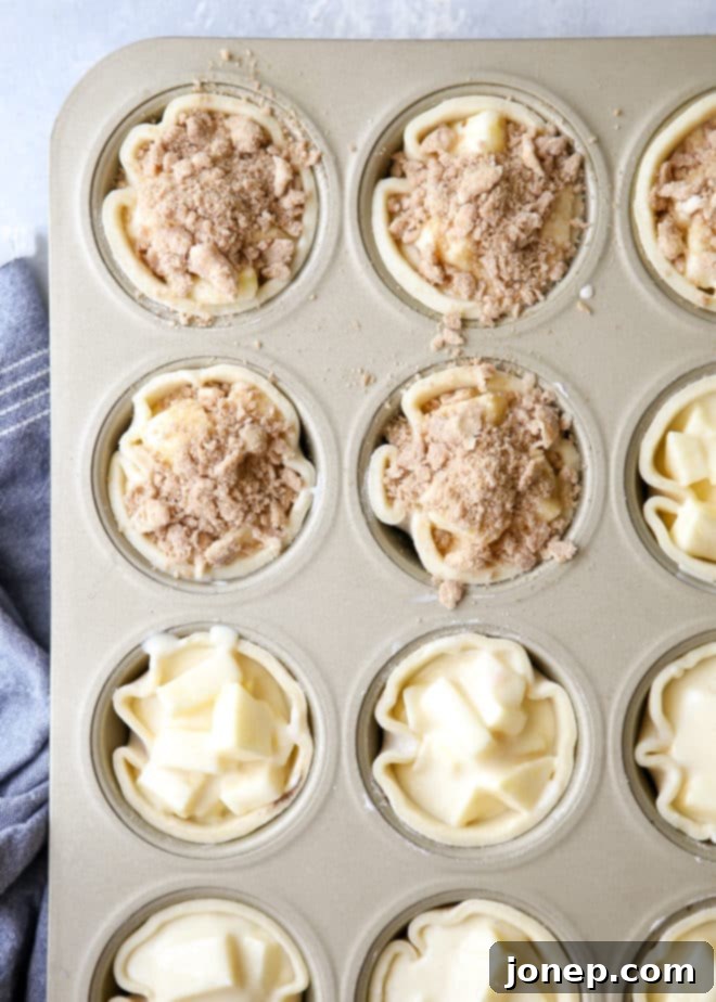 A top-down view of several mini sour cream apple pies, with one pie showing a fork inserted into it, revealing the apple and sour cream filling.