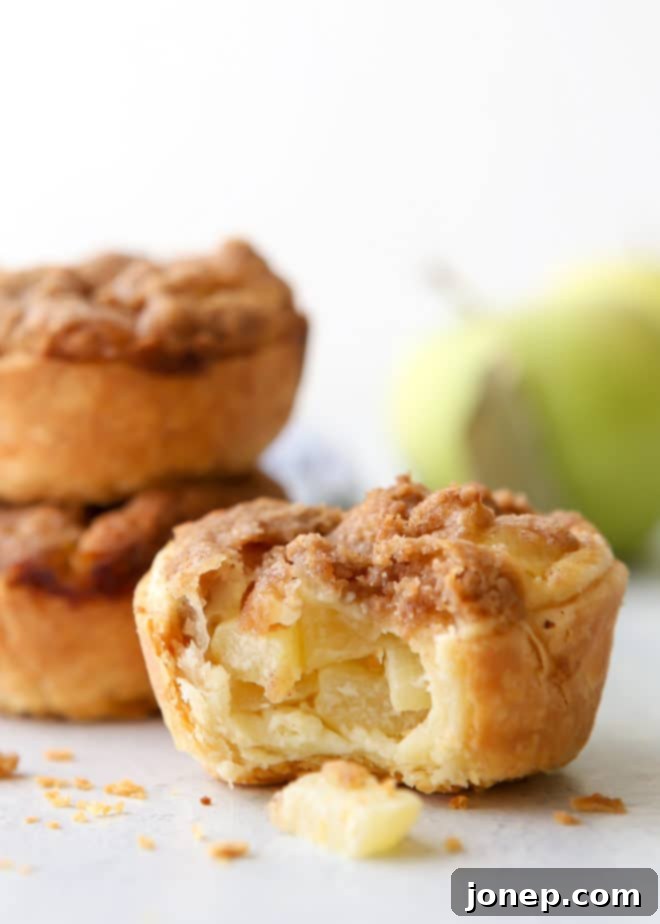 Several mini sour cream apple pies cooling on a wire rack, with a rustic background.