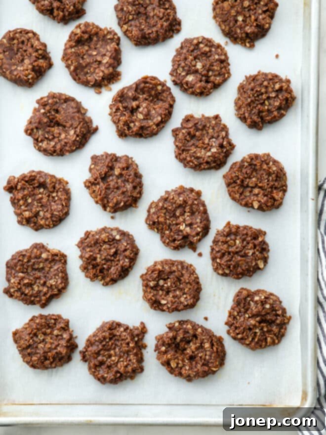 A baking sheet covered with parchment paper, displaying multiple freshly scooped no-bake chocolate cookies cooling and setting.