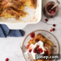 baked french toast on a plate with whipped cream and cranberry maple syrup