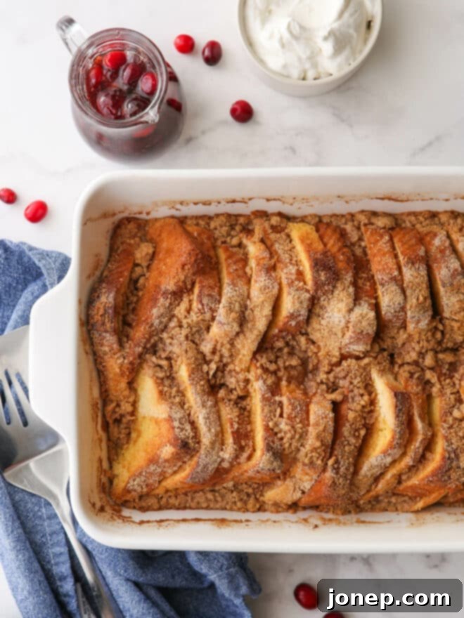 baked french toast in pan with pitcher of syrup and whipped cream