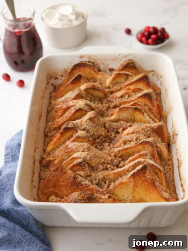baked french toast in pan with pitcher of syrup and whipped cream