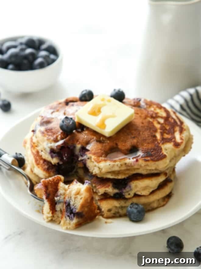 Blueberry Buttermilk Bliss 8 Stack of blueberry pancakes with a bite taken out by a fork, showing the fluffy interior and juicy berries