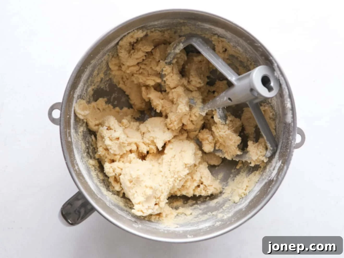 Close-up of fluffy sugar cookie dough in a mixing bowl with a paddle attachment.