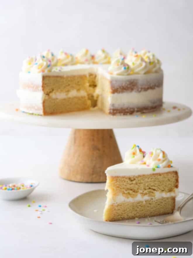 Frosted Sugar Cookie Cake 10 A delectable slice of sugar cookie layer cake with the full cake in the blurred background, showcasing its delicious layers.