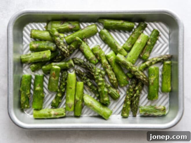 Chopped asparagus spears seasoned with olive oil, salt, and pepper, spread evenly on a sheet pan, ready for the oven