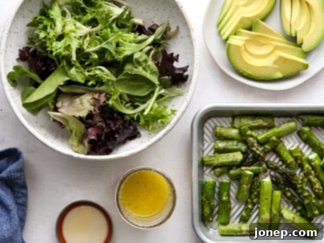 All vibrant components of the roasted asparagus avocado salad including dressed greens, perfectly roasted asparagus, and freshly sliced avocado, artfully arranged in a bowl