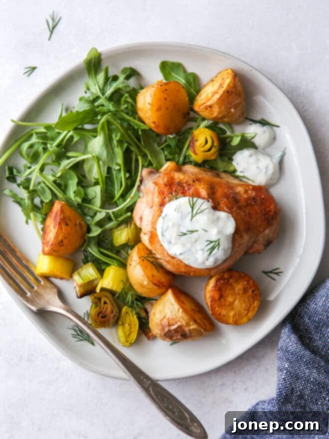 Sheet Pan Roasted Chicken with Potatoes and Leeks 7 A serving of one-pan roasted chicken, potatoes, and leeks on a plate, topped with creamy dill sauce and fresh dill, next to a bowl of arugula