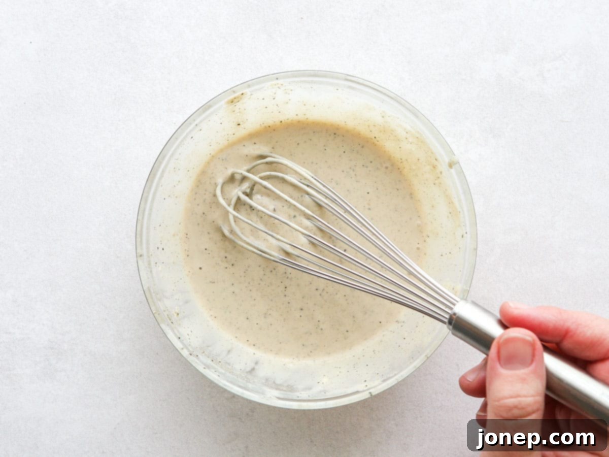 Whisking creamy homemade Caesar dressing in a bowl, a key step for the Chicken Caesar Pasta Salad recipe.