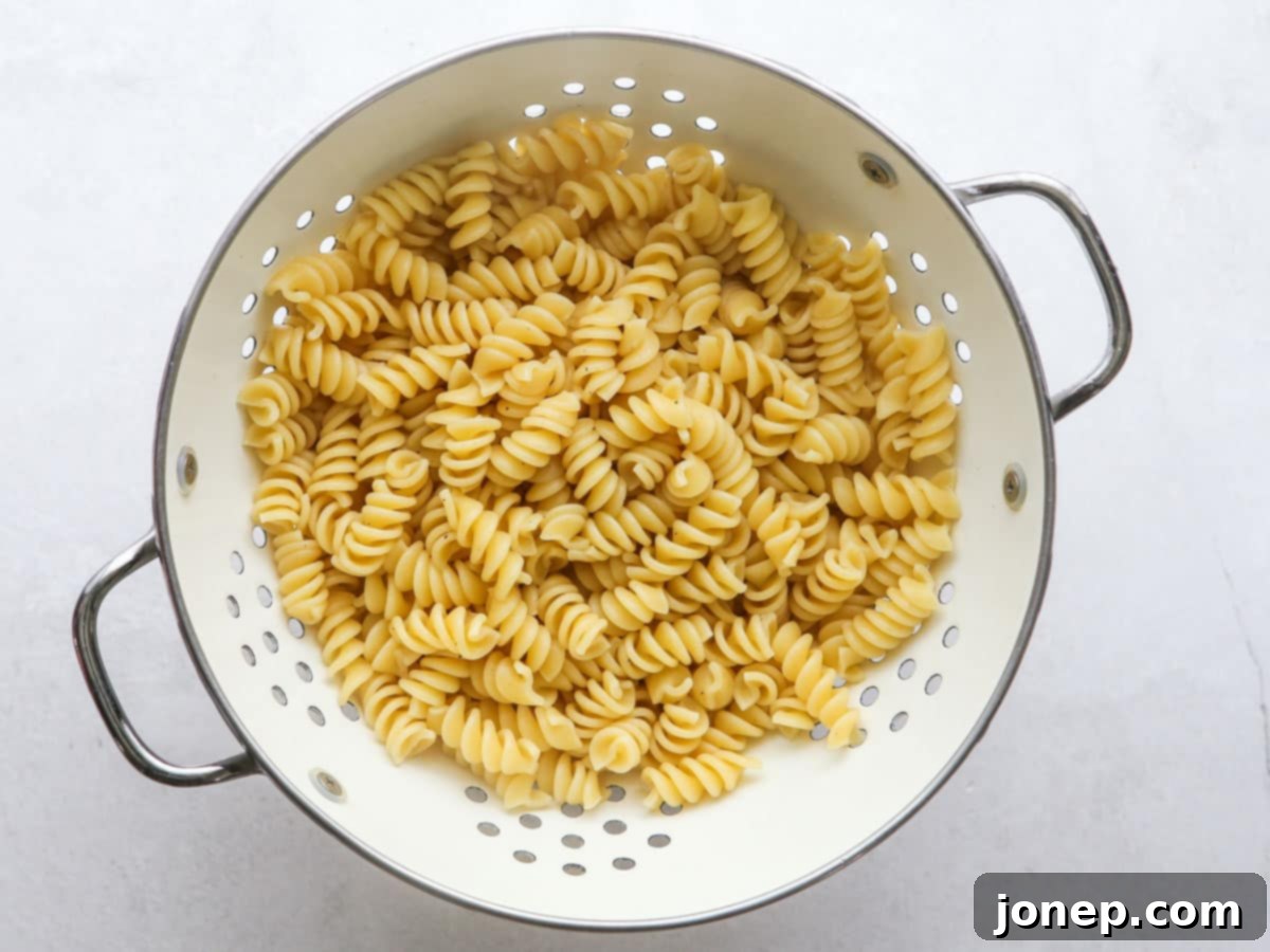 Freshly drained, al dente cooked rotini pasta in a colander, ready to be cooled for Chicken Caesar Pasta Salad.