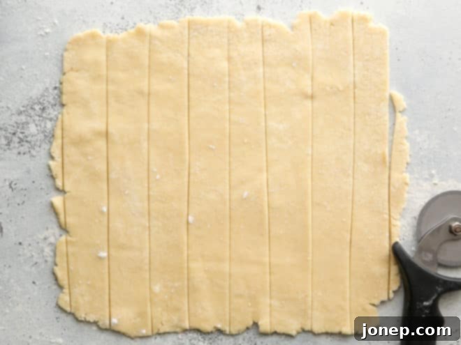 Sections of pie crust dough neatly cut into even strips, organized on a floured surface, ready for the lattice weaving process.