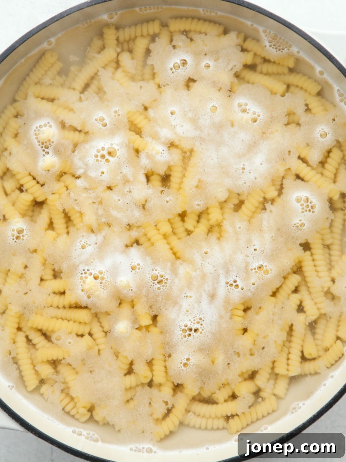 Smoky Creamy Grilled Corn Pasta 6 Short pasta cooking in a pot filled with water on a stove, using the cold water start method