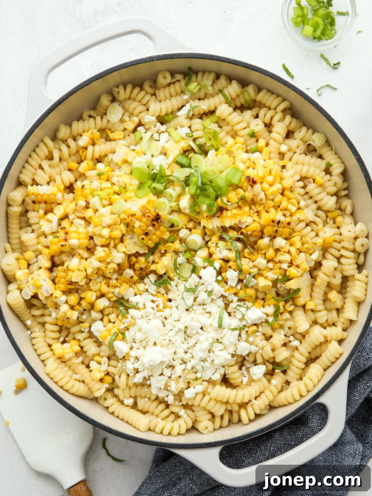 Smoky Creamy Grilled Corn Pasta 7 Mixing cooked pasta with grilled corn, crumbled feta, chopped green onions, and fresh basil in a large pot