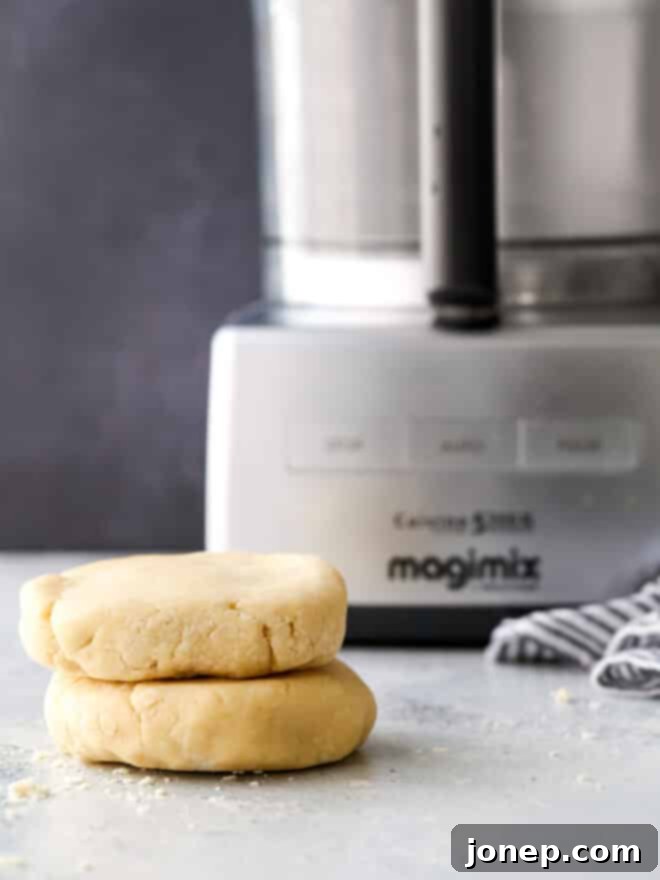 Effortless Food Processor Pie Crust 2 Perfectly formed pie crust disks ready for chilling, with a food processor in the background.