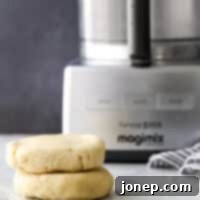 Effortless Food Processor Pie Crust 11 Two disks of pie crust dough next to a food processor, highlighting the ease of making homemade pie crust.