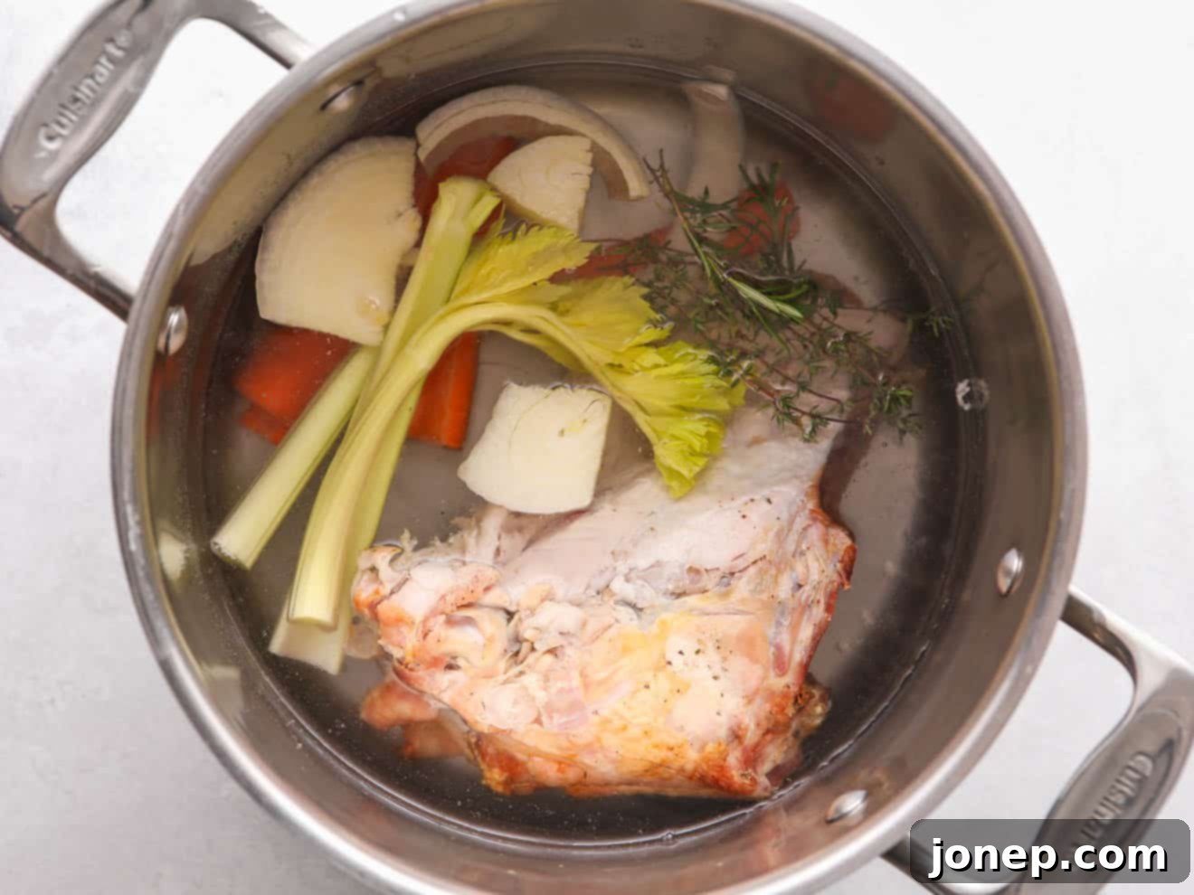 Adding turkey bones, chopped onions, carrots, and herbs to a large stock pot, covered with cold water, to make homemade broth.