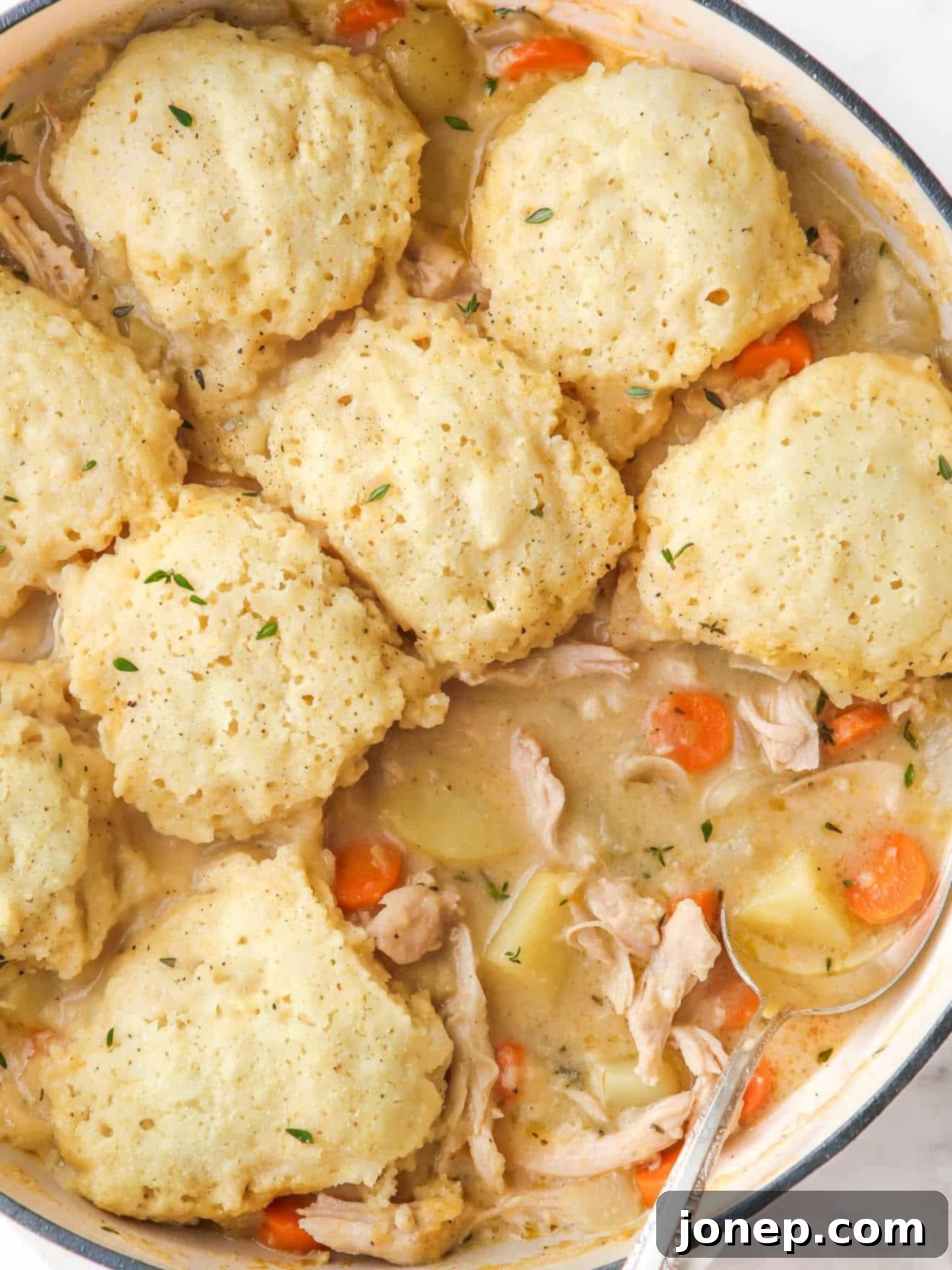Close-up of fluffy buttermilk dumplings simmering on top of a hearty turkey soup in a large pot, indicating they are almost cooked.