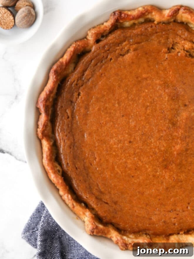 A whole classic pumpkin pie cooling on a wire rack, steam gently rising, showcasing its perfect golden-brown crust.