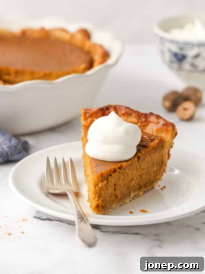 A close-up of a slice of classic pumpkin pie on a white plate, garnished with generous swirls of homemade whipped cream and a hint of spice.