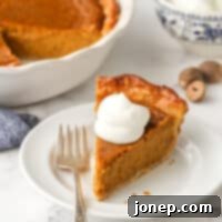 Classic Pumpkin Pie with whipped cream and a sprinkle of cinnamon, served on a white plate with a fork.