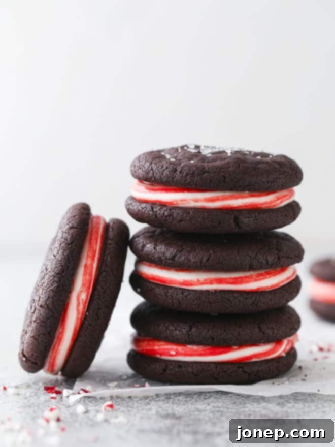 A close-up of several chocolate candy cane cookies stacked on top of each other, highlighting the swirled red and white frosting