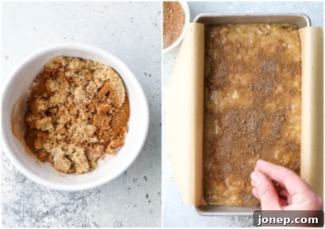 Banana bread batter being spread into a loaf pan, topped with a generous sprinkle of cinnamon crumble.