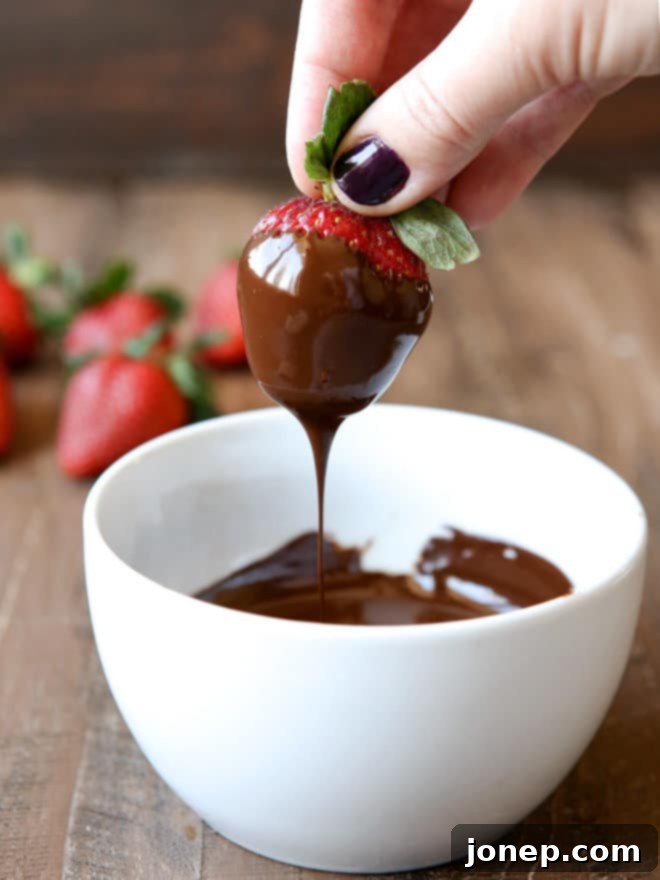 Close-up of a hand dipping a fresh strawberry into melted chocolate, showing the smooth, rich coating.