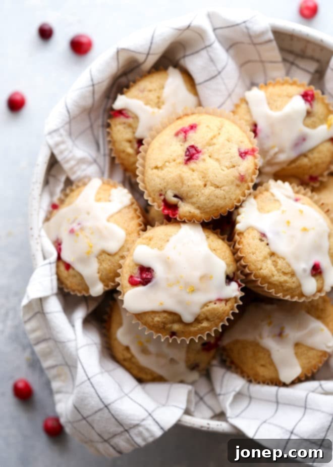 Soft and buttery, these cranberry orange muffins are bursting with flavor in every bite! A stack of three glazed cranberry orange muffins on a serving plate.