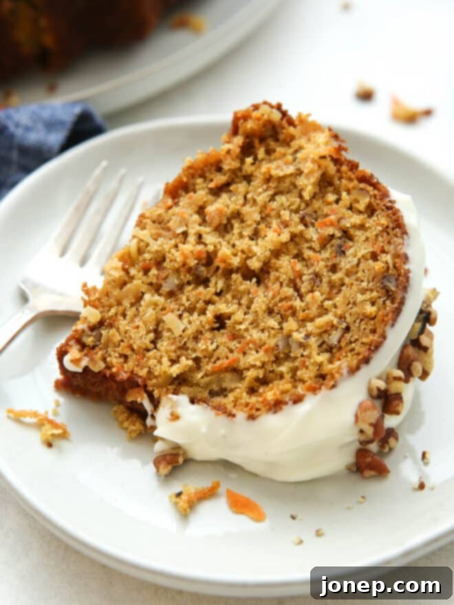 Golden Spiced Carrot Bundt 3 A close-up shot of a slice of moist carrot bundt cake showing the texture, visible carrots, pecans, and coconut, topped with cream cheese frosting.