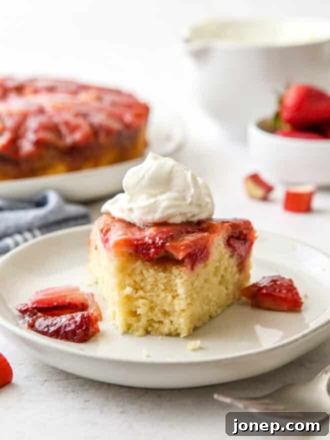 Strawberry Rhubarb Flip Cake 9 A slice of Strawberry Rhubarb Upside-Down Cake served on a plate with whipped cream, garnished with fresh mint.
