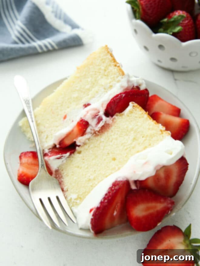 Strawberry Shortcake Cloud Cake 3 Close-up of a perfect slice of strawberry shortcake layer cake on a white plate, showcasing the fluffy cake, thick whipped cream, and juicy strawberries.