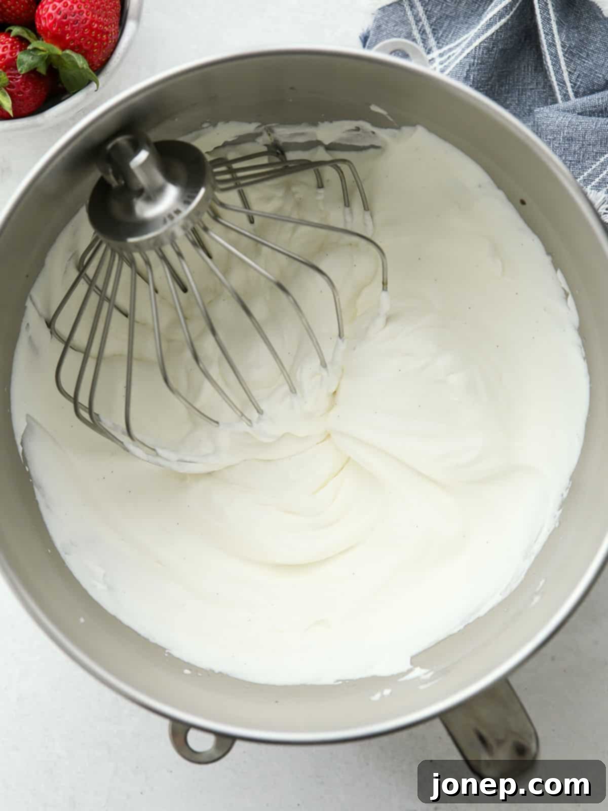 Electric mixer whisking cold heavy cream, sugar, and vanilla to create fluffy whipped cream for strawberry shortcake.