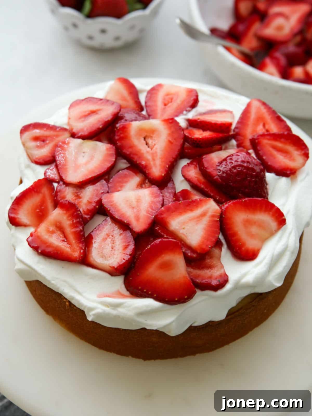 Assembly in progress: a layer of vanilla cake topped with a thick layer of whipped cream and sliced macerated strawberries, ready for the next cake layer.