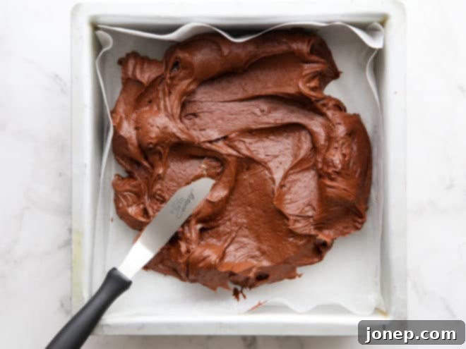 Spreading smooth peppermint fudge mixture into a parchment-lined pan, ready for chilling