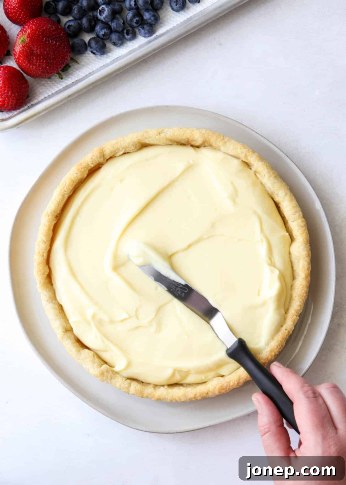 Step-by-step image showing the assembled tart with lemon filling and fresh berries, ready to chill.