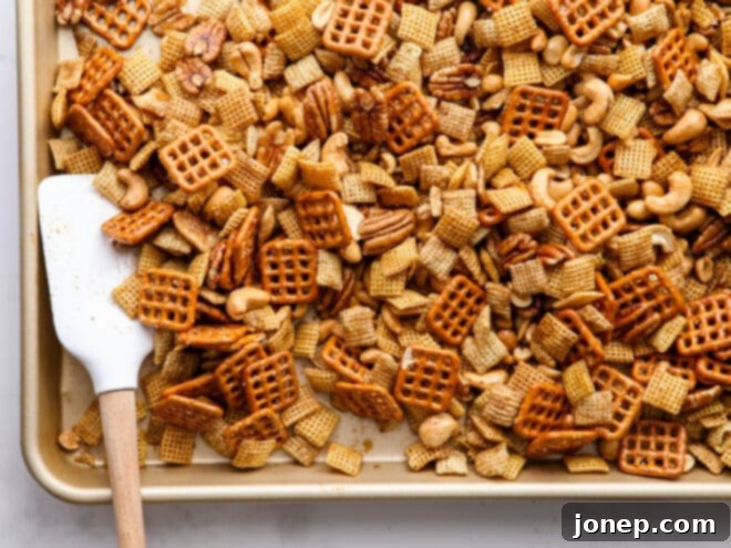 Stirring the snack mix on a baking sheet to ensure even coating during baking