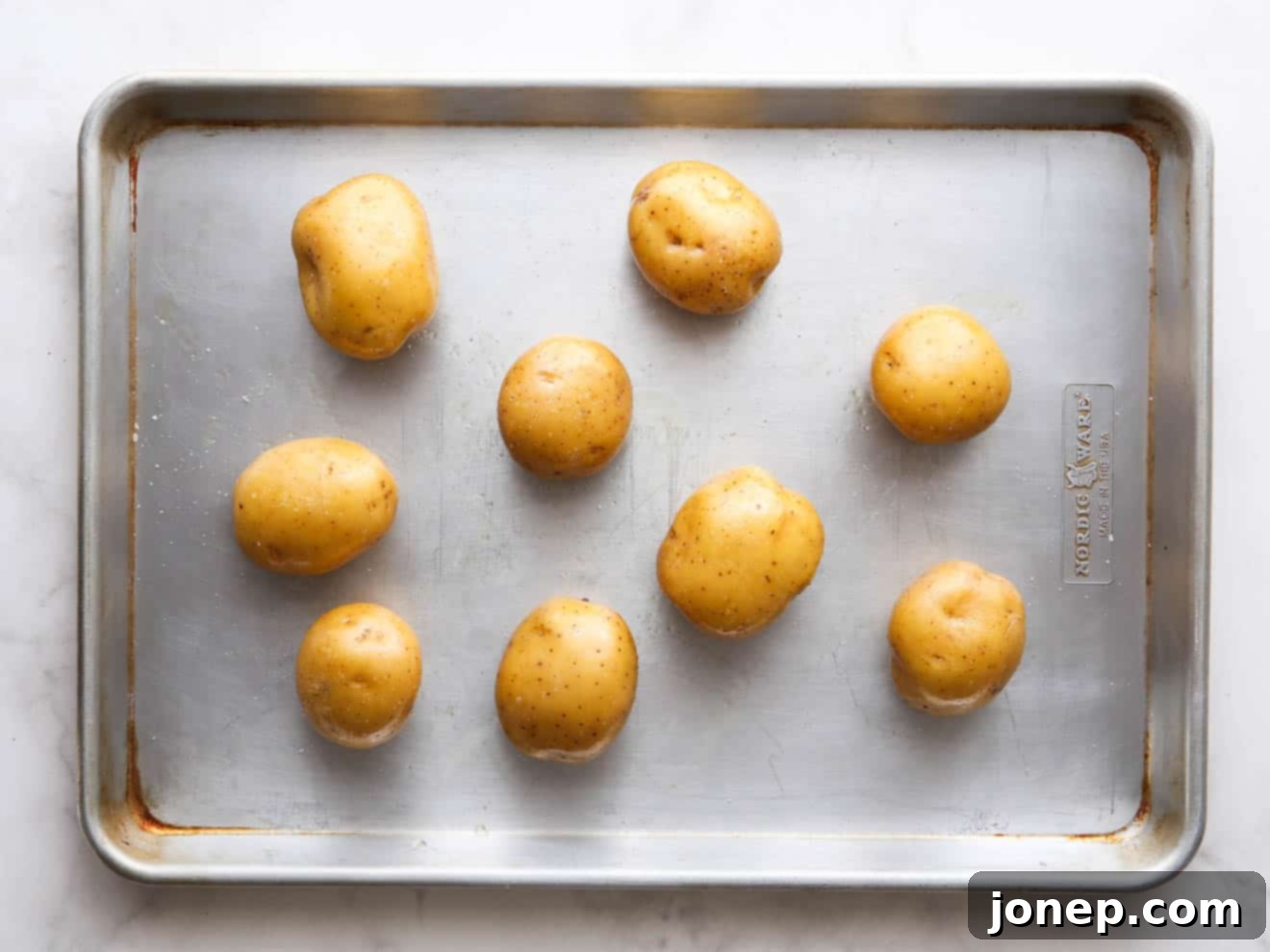Potatoes on a sheet pan ready for roasting, evenly spaced and seasoned.