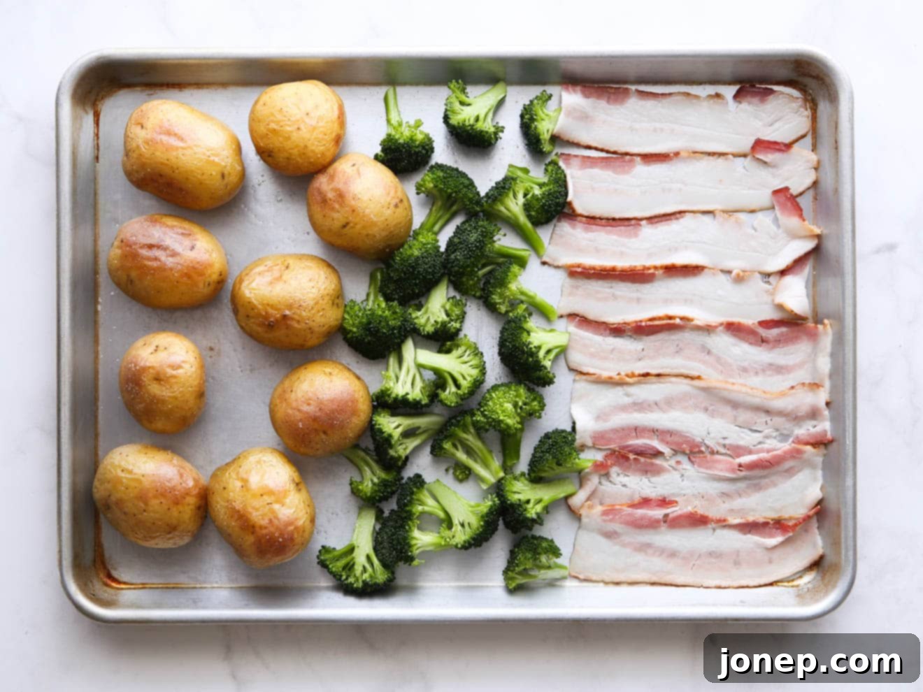 Adding broccoli and bacon to the sheet pan alongside partially roasted potatoes.
