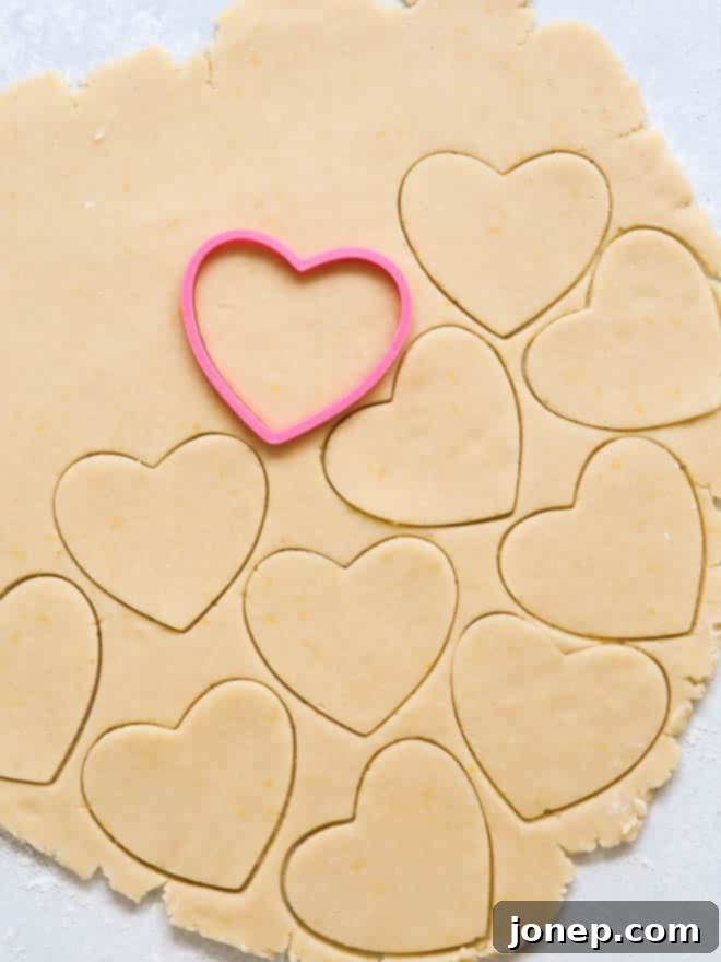 Hands rolling out cookie dough and cutting shapes with cookie cutters