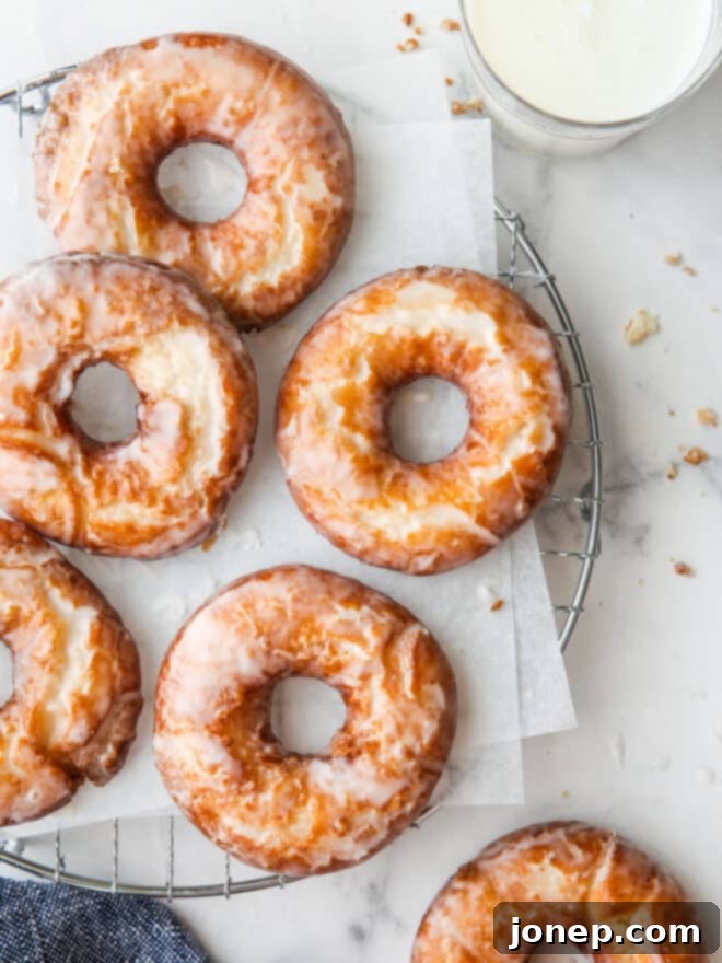 Glazed old-fashioned buttermilk doughnuts cooling on a wire rack with a glass of milk beside them.